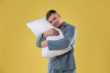 Man in stylish pajamas with pillow on yellow background