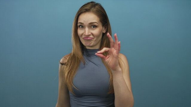Woman finger pointing and showing ok sign with quizzical smirk and raised eyebrow in blue studio; skepticism.