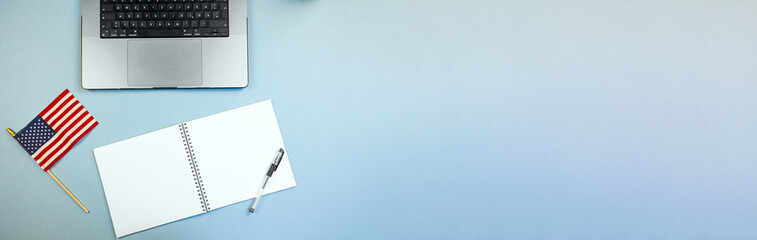 national banner with tech devices, stars and stripes alongside electronic gadgets on workspace table, american flag displayed near laptop and journal on vibrant blue desk for planning