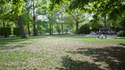 Blurred scene of people in a lush green park with bokeh effect showcasing defocused backgrounds and flowers creating a serene atmosphere.