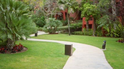 Fototapeta premium Defocused tropical resort path with lush greenery and palm trees creating a serene luxury atmosphere in an outdoor hotel setting.