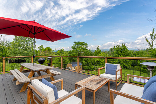 Spacious wooden deck with outdoor seating, picnic table and red umbrella overlooking green landscape