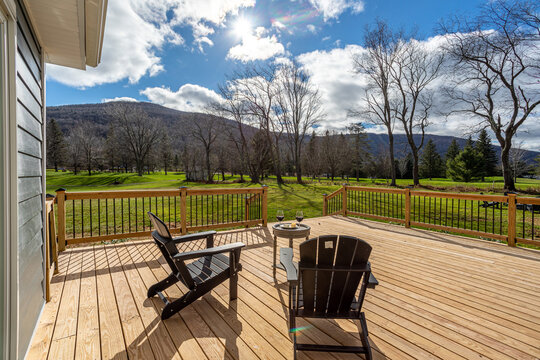 Wooden deck with outdoor chairs overlooking green valley and mountains on sunny d