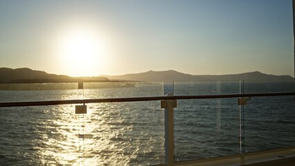 Obraz premium Glass balcony railing and sunlit ocean with distant islands in soft bokeh outdoor background, shallow focus on glass panel; background copyspace backplate template.