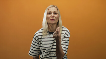 Fototapeta premium Woman beckons with fingers toward camera and later visibly rubs forehead in orange studio; plea frustration.