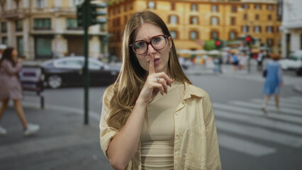 Fototapeta premium Woman with raised index finger pressed to lips gestures silence on a bustling city street, surrounded by blurred pedestrians; hush secrecy mystery calm.