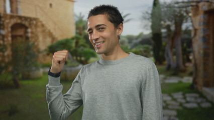 Fototapeta premium Man in grey sweater winks eye and points thumb at historic old town building courtyard outdoors; confidence.