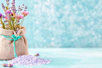 Natural bath sea salt in rustic fabric pouch with lavender and wildflowers, blue salt crystals scattered below. Spa relaxation concept with large copy space for wellness branding and packaging.