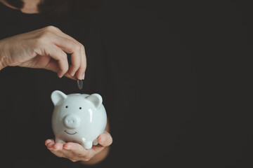 Woman hand putting coin into white piggy bank, saving money concept for financial planning, personal budget, investment growth, retirement fund and smart saving for future financial security.