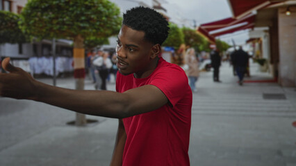 Fototapeta premium Man lifts hand and points finger in a busy city street scene with blurred pedestrians and urban storefronts; confidence.