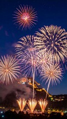 Night sky filled with bright, colorful fireworks over a hillside building