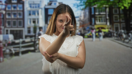 Fototapeta premium Woman making finger to lips and a pointing gesture on street in front of canal houses with uncovered fingers and forearm visible; silence secrecy.