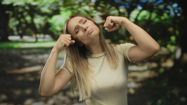 Young woman making funny crying faces outdoors in park setting during daytime surrounded by green trees wearing casual clothing captured mid laugh and expression change