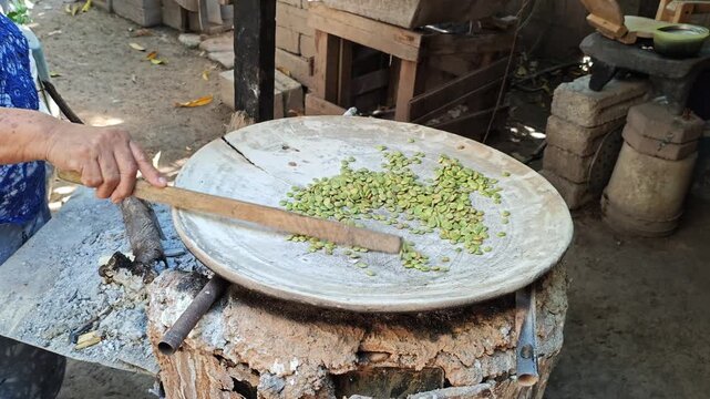 Woman roasting guaje seeds (Leucaena) on a traditional clay comal over a wood fire.