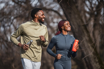 African american couple jogging outdoors, staying hydrated