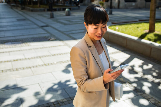 Smiling businesswoman checking smartphone on city street