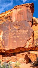 Ornate canyon wall with ancient petroglyphs under a partly cloudy, bright, blue sky