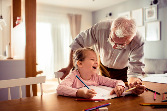 Grandfather helping granddaughter with drawing at home