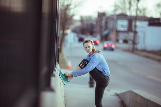 Young woman stretching before run on urban sidewalk
