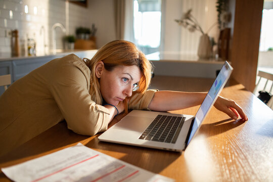 Tired woman with burnout working on laptop at home kitchen table