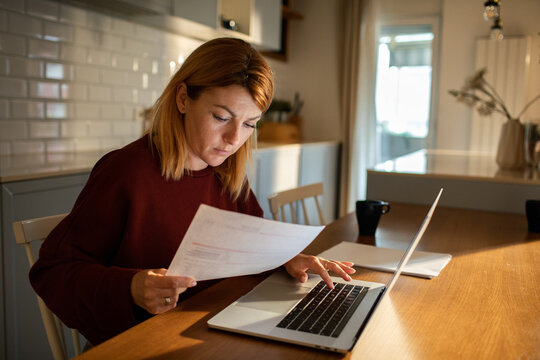 Woman reviewing bills on laptop in home kitchen