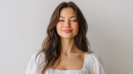 Naklejka premium Serene young woman with long hair in white shirt smiling softly against a neutral background capturing a moment of tranquility and joyfulness in life