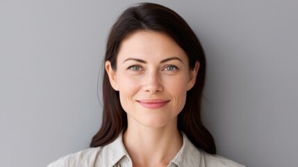 Fototapeta premium Female Portrait with Natural Smile Against Gray Background, Showcasing Confidence and Approachability in Casual Attire
