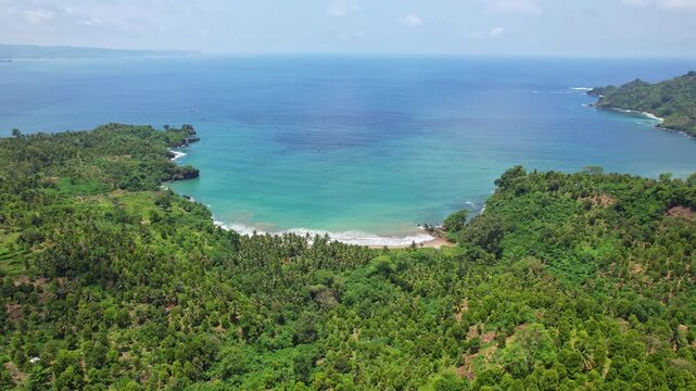 Aerial drone footage of a white bay beach nearby Jalan Lintas Selatan, a new coastal road on the south coast of Java island, Trenggalek regency, Indonesia, with blue coral sea in sunny weather