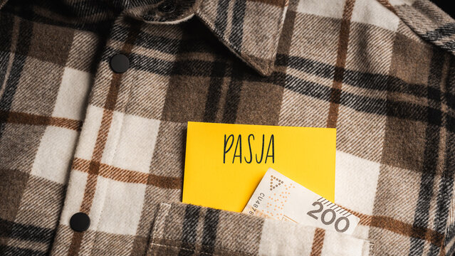 Yellow card with a handwritten inscription "Pasja\
", protruding from a brown plaid shirt, next to Polish banknotes PLN (selective focus)