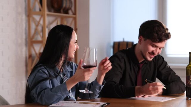 Professional sommeliers with glass of red wine filling out tasting card at table indoors