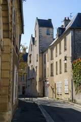 Obraz premium Sunlit narrow European street with charming old buildings, showcasing architectural details, shuttered windows, and a dynamic play of light and shadow.