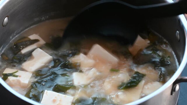 Stirring Japanese Miso Soup with Soft Tofu and Wakame Seaweed in a Boiling Pot using a Ladle