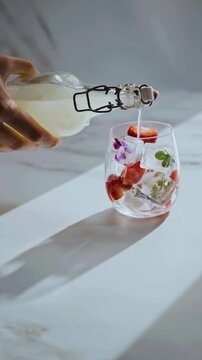 Pouring Fresh Lemonade into Glass with Floral Ice Cubes and Strawberries