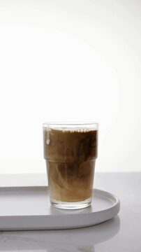 Pouring Fresh Milk into a Glass of Black Coffee on White Background