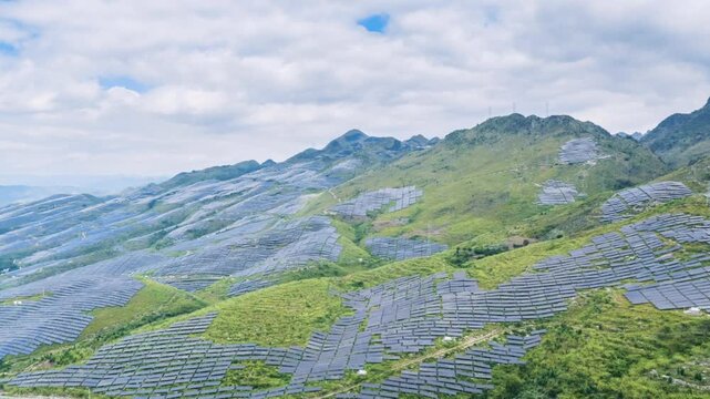Aerial time-lapse of a solar power station on rocky desertified hills, with rows of photovoltaic panels spread across green slopes, new energy transforming degraded land.