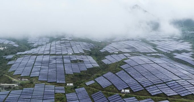 Aerial footage of solar power station on rocky hills under misty clouds, renewable energy in mountainous terrain.