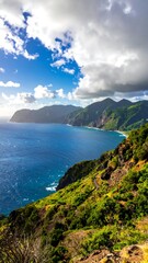 Fototapeta premium Lush green hills meet the deep blue sea under a partly cloudy, bright sky