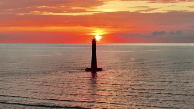 Aerial view of Morris Island Lighthouse and morning colorful orange sun along ocean horizon on Folly Beach near Charleston, South Carolina landscape seascape during sunrise - 4K Drone