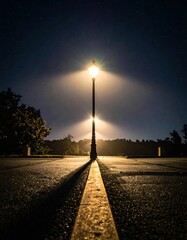 Illuminated street lamp emits a strong, centered glow on a road under a starry night sky