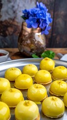 Glazed yellow cakes sit on silver tray, a vase of blue flowers behind