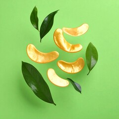 Golden eye patches amid glossy green leaves on a bright green background, suggesting skincare and freshness