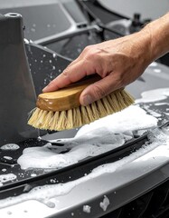 Hand brushes foamy cleanser across a car's textured hood in a close-up view, detailing the wash
