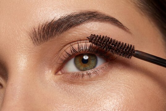 Close up detail of young woman applying mascara to eyelashes with brush showing natural skin texture
