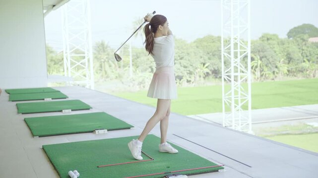 Golf instructor teaching swing technique to Asian woman at driving range