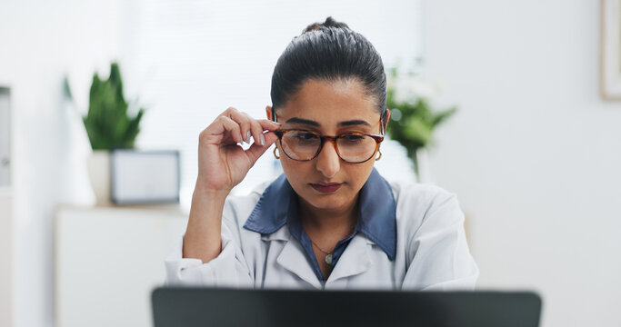 Glasses, healthcare and laptop with doctor in office at hospital for online planning or research. Computer, medical and reading with Indian woman in clinic for administration, report or study
