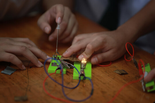 Curious hands working simple electrical circuit experiment diy science for kids project glowing light bulb shows success and excitement learning