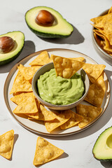 Delicious avocado guacamole served with crispy tortilla chips on a plate with fresh avocados scattered around