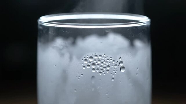 Close up of bubbling liquid in a glass beaker with steam rising.