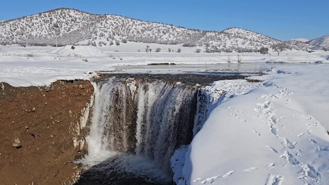 A winter waterfall drops from a snowy plain into a deep canyon, framed by distant Zagros mountains and forests surrounding the untouched white landscape.
📍Marivan, Kurdistan 