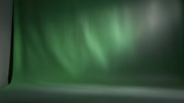 Green seamless backdrop in a shadowed studio corner creating a soft, moody greenscreen ambiance